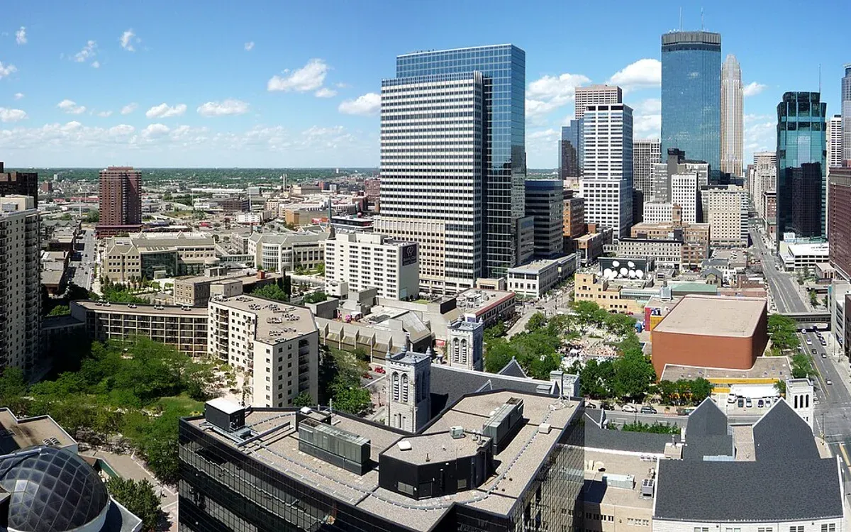 A wide panoramic view of the downtown Minneapolis skyline, including the IDS Center, Wells Fargo Center, and Capella Tower