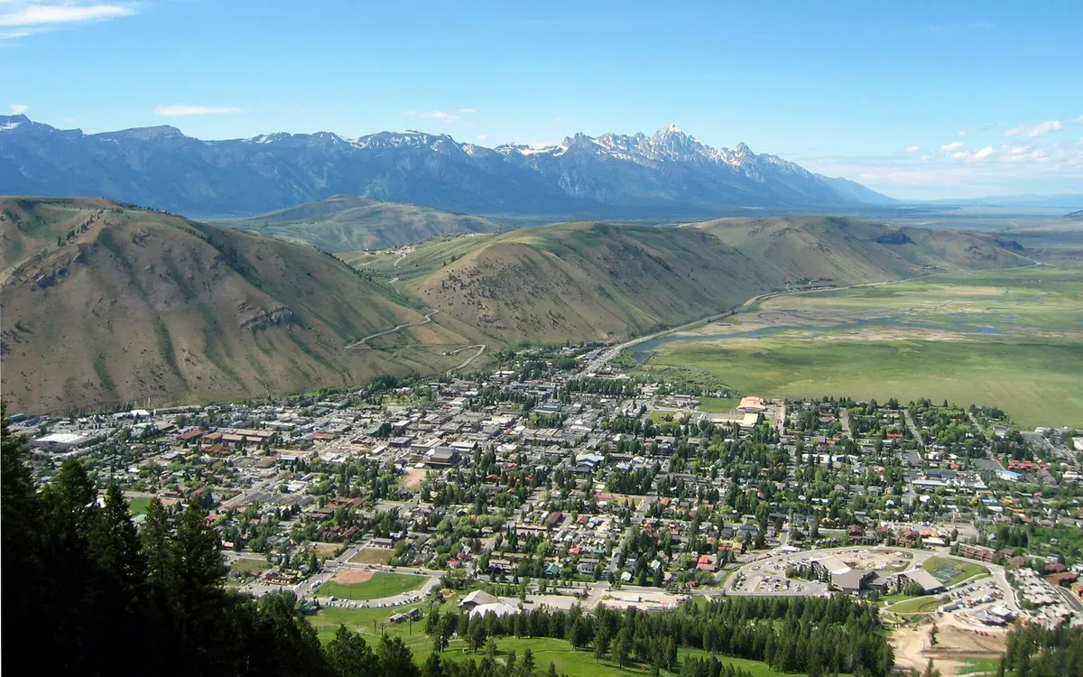 An elevated view of the town of Jackson, Wyoming filling a mountain valley, with the Grand Teton range visible on the skyline behind it